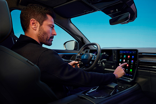 Kuvassa mies istuu kuljettajan paikalla pitäen kiinni ratista toisella kädellä ja koskettaa sormella openR-näyttöä.