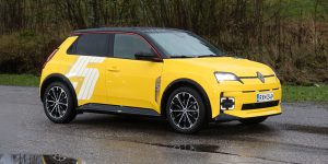 Keltainen Renault 5 E-Tech electric sivusta kuvattuna sateisessa maisemassa.